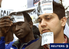 2 extranjeros manifestándose y con pegatinas en la cara en contra de la Ley de Extranjería
