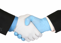 Dos personas dándose la mano y cada una tiene cubierta su mano con un guante de plástico uno azul y otro blanco