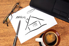 La labor del abogado en el derecho inmobiliario Dibujo de una casita, un boli, unas gafas y un café sobre una mesa