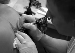 Una persona haciendo un tatuaje en la espalda a otra. Una persona haciendo un tatuaje en la espalda a otra.